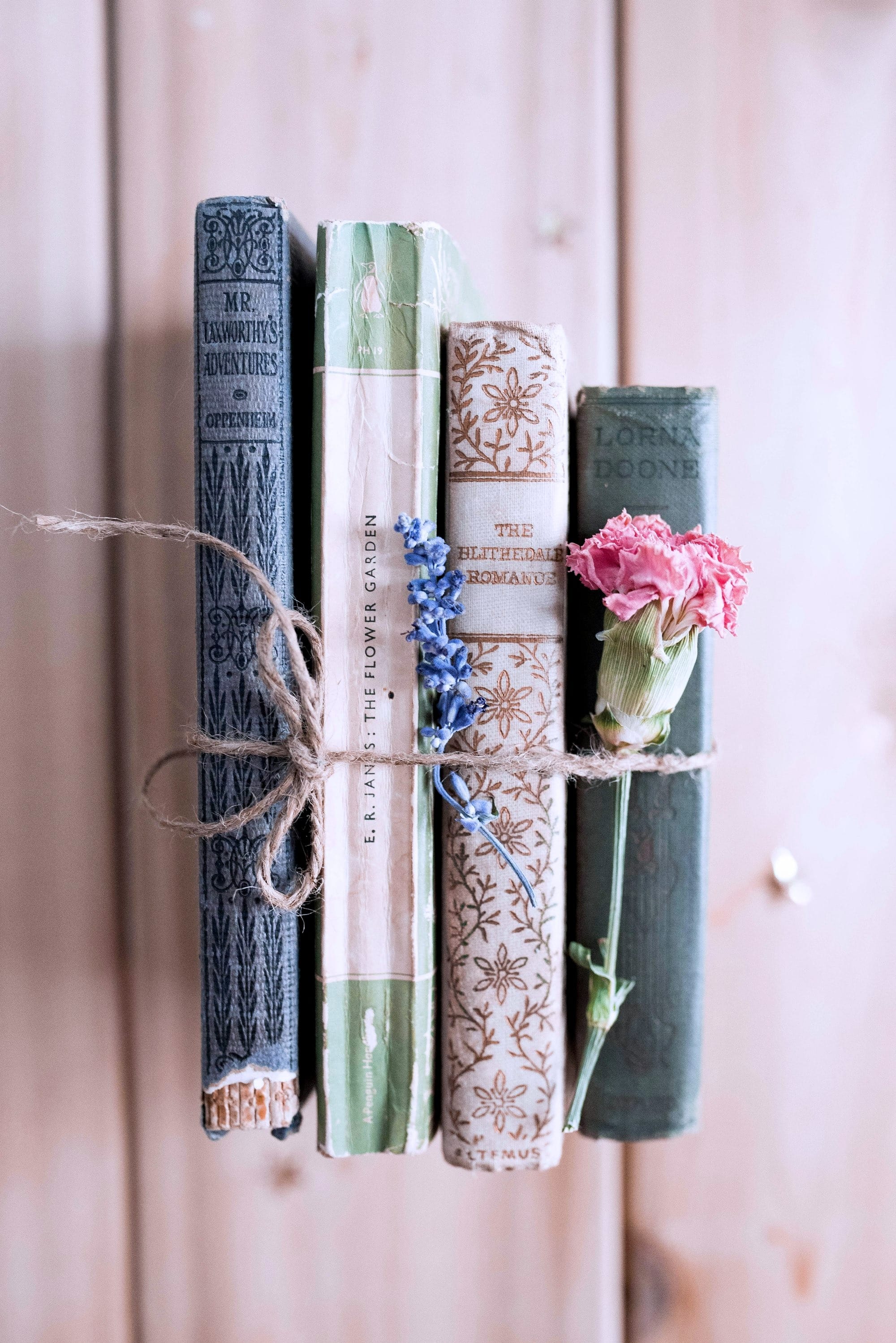 Four aged books, spines facing the viewer, and two flowers tied together with twine.
